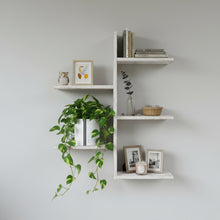 White shelves with decorative items including a plant, books, and framed pictures on a light gray wall.