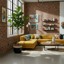 Modern living room with yellow sectional sofa, brick wall, and decorative elements.