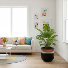 Modern living room with a white sofa, colorful cushions, a plant in a striped pot, and abstract art on the wall.
