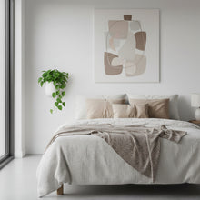 Neatly made bed with beige bedding and abstract art on the wall in a bedroom.