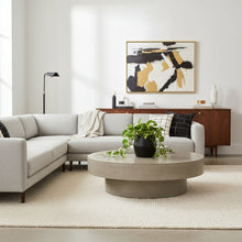 Modern living room with a gray sectional sofa, round coffee table, and abstract art on the wall.