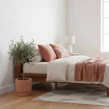 Bedroom with wooden bed, pink pillows, and a plant on a white wall.