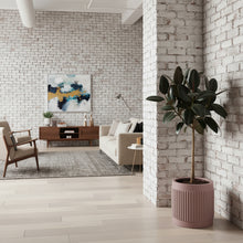 Modern living room with white brick walls, a sofa, armchair, and a potted plant.