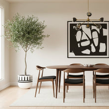 Dining room with wooden table and chairs, abstract art on the wall, and a potted plant.