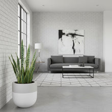 Modern living room with a gray sofa, plant, and abstract art on a white brick wall.
