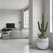 Modern living room with white brick walls, a gray sofa, and a potted cactus.