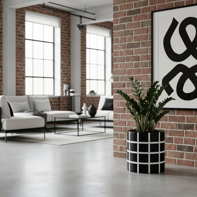 Modern living room with white sofa, black and white patterned plant pot, and abstract art on brick wall.