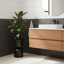 Modern bathroom with wooden vanity, white sink, and black plant pot.
