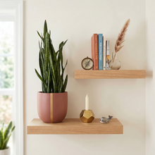 Wooden shelves with a rust plant pot with vertical gold stripe, books, and decorative items against a light wall.