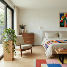 Modern bedroom with a bed, chair, dresser, and colorful rug.