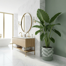 Modern bathroom with oak vanity, round mirror, and potted plant.  Large soaker tub in front of window