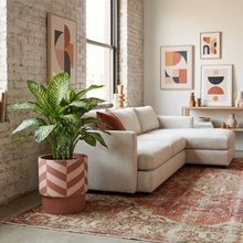 Modern living room with a beige sectional sofa, decorative planter with dieffenbachia plant, and abstract art on a brick wall.