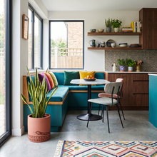 Modern kitchen and dining area with teal sofa, wooden shelves, and colourful decor.