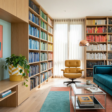 Modern library with bookshelves, a yellow armchair, and a teal sofa.