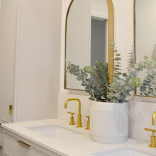 Bathroom vanity with gold fixtures, white sink, and decorative plants.