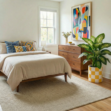 Neatly arranged bedroom with a bed, dresser, and decorative plant.