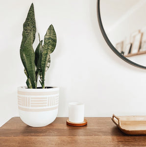 white flower pot with subtle design with candle beside it and a round mirror in background