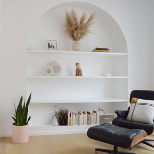 soft pink cylinder placed on floor in front of arched built-in shelving