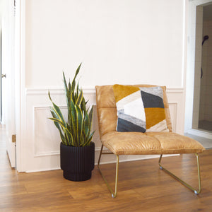a tobacco colour leather accent chair with brass legs with woven wool cushion.  A black scallop cylinder planter on floor beside chair.  Large plant pots are perfect for keeping on the floor next to the fireplace, for adding into corners or long hallways for an aesthetic look. Hand painted minimal planters
