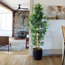 Black scallop cylinder pot sits on floor with a framed scenic art print on the wall behind it.  In the distance, a stone fireplace and stove, with a tobacco shay leather accent chair and black ceiling fan.  Minimalist plant pot perfect for new and mature plants and florals. Hand painted, lightweight and modern.