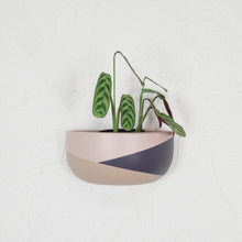 A color block short wall planter baked clay pot with a plant growing out of it, mounted on a wall.