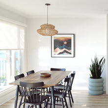 Walnut kitchen table with black wooden dining chairs.  A rattan hanging chandelier hangs over table.  An artwork print hangs on back wall of dining room.  A sage green ring stacked flower pot sits on floor in corner of dining room. 