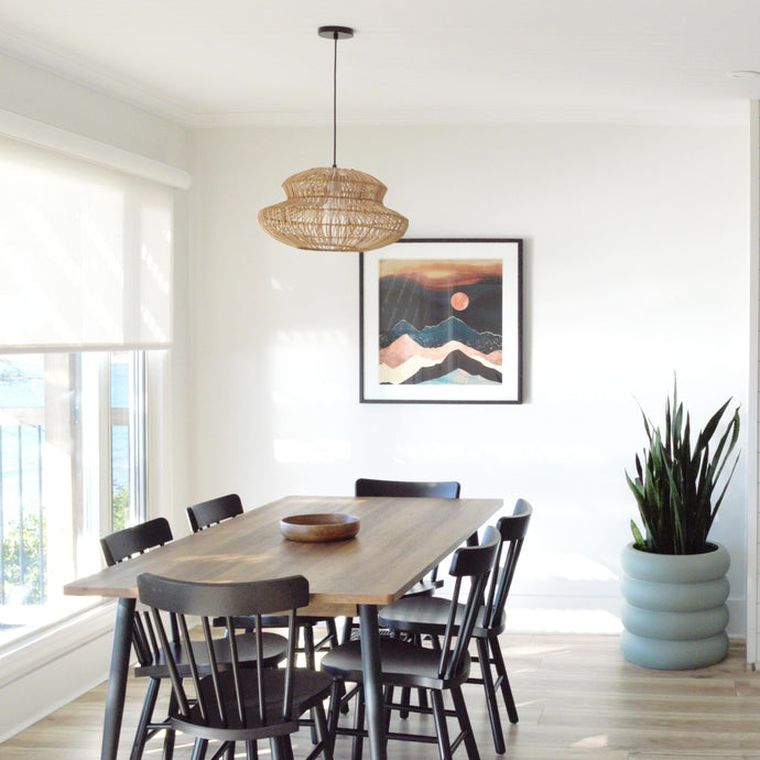 Four cane side chairs placed around a round marble table.  A rattan hanging pendant hangs above table.  An H&M donut vase is placed on centre of table with natural dried palm leaves.  A cream coloured, tiered, ring stacked planter pot sits in the corner holding a fiddle leaf fig plant.  Warm sunlight fills the room from the left side. Plants are powerful.