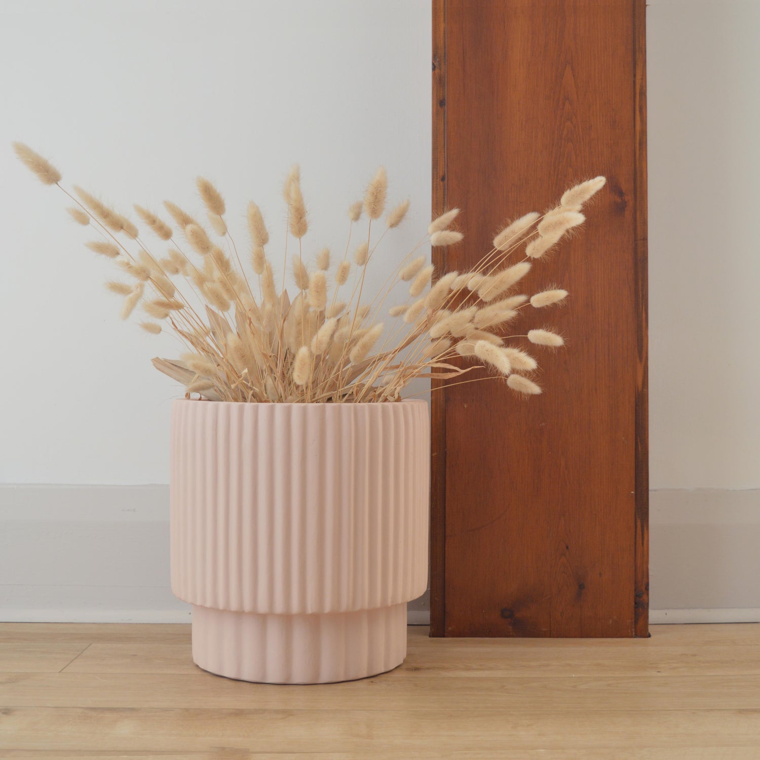 Soft pink scalloped cylinder placed on floor with dried, natural rabbit tails.  