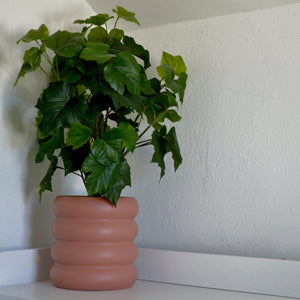 terracotta coloured areaware ring stacked planter pot with fake plant on white counter top.